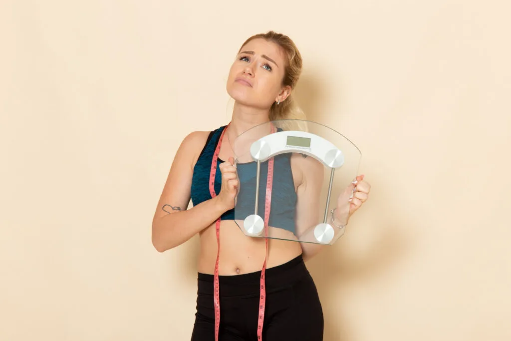 Why Am I Not Gaining Weight Even After Exercising? (10 Reasons & Fixes) 2 Why am I not gaining weight after exercising? Woman holding a weighing machine and checking her weight.