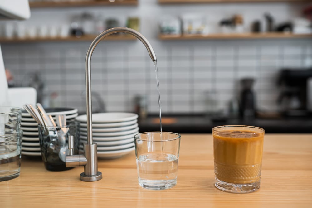 Glass of water and glass of coffee side by side on a morning table, illustrating the health impact of drinking coffee before water.